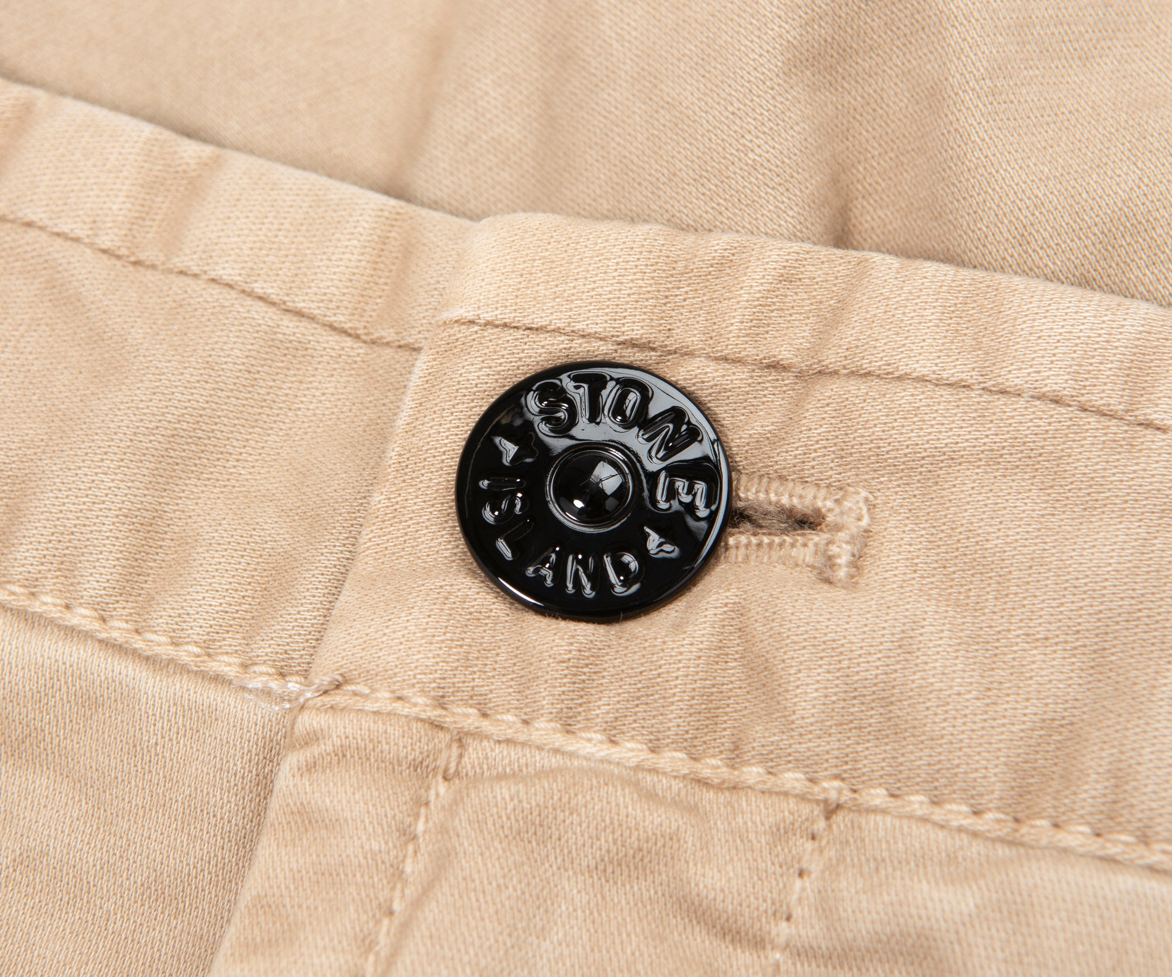 Close-up of a beige fabric with a black button featuring 'Stone Island' branding.