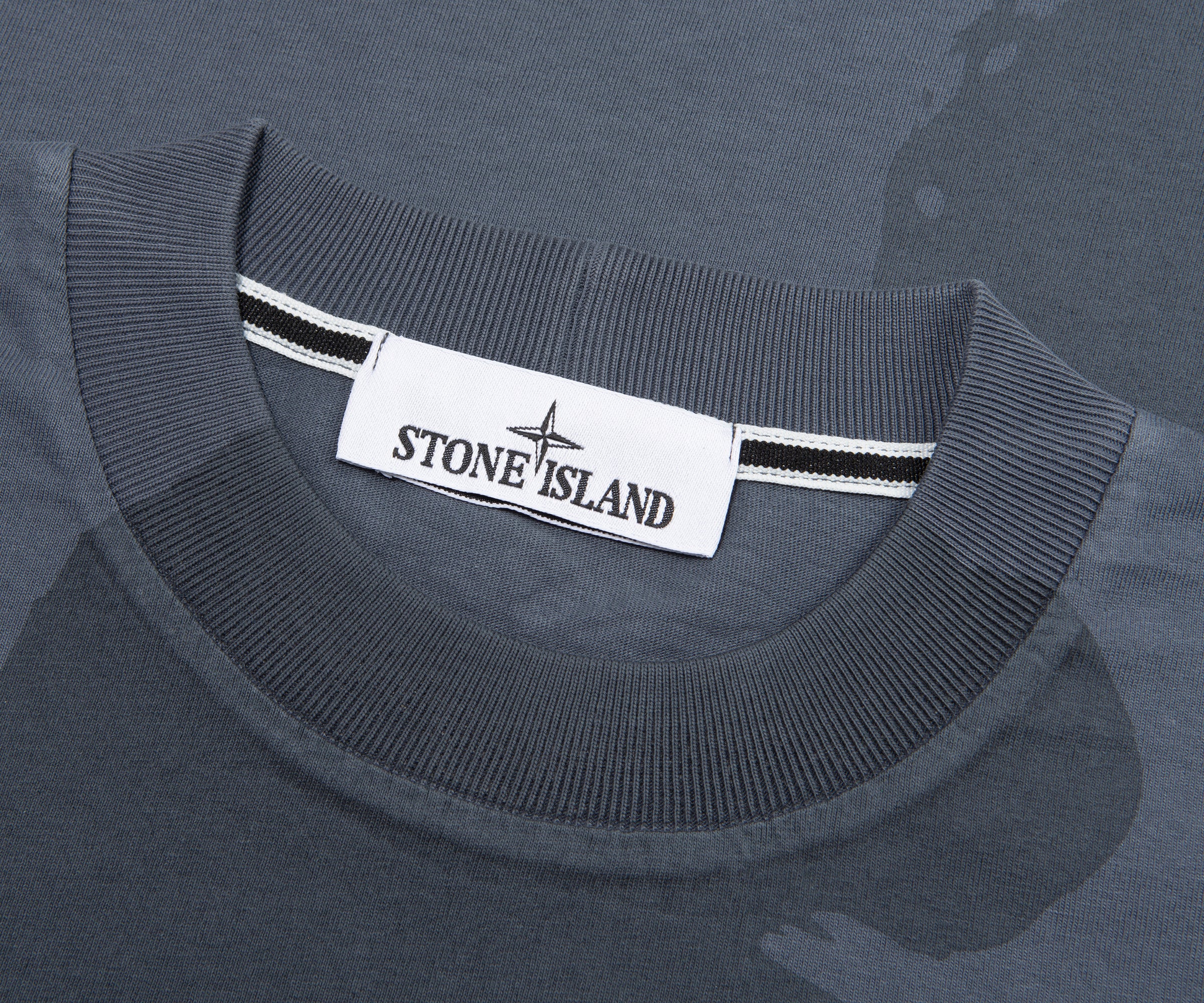 Close-up of a gray sweater with a Stone Island label on a matching gray background