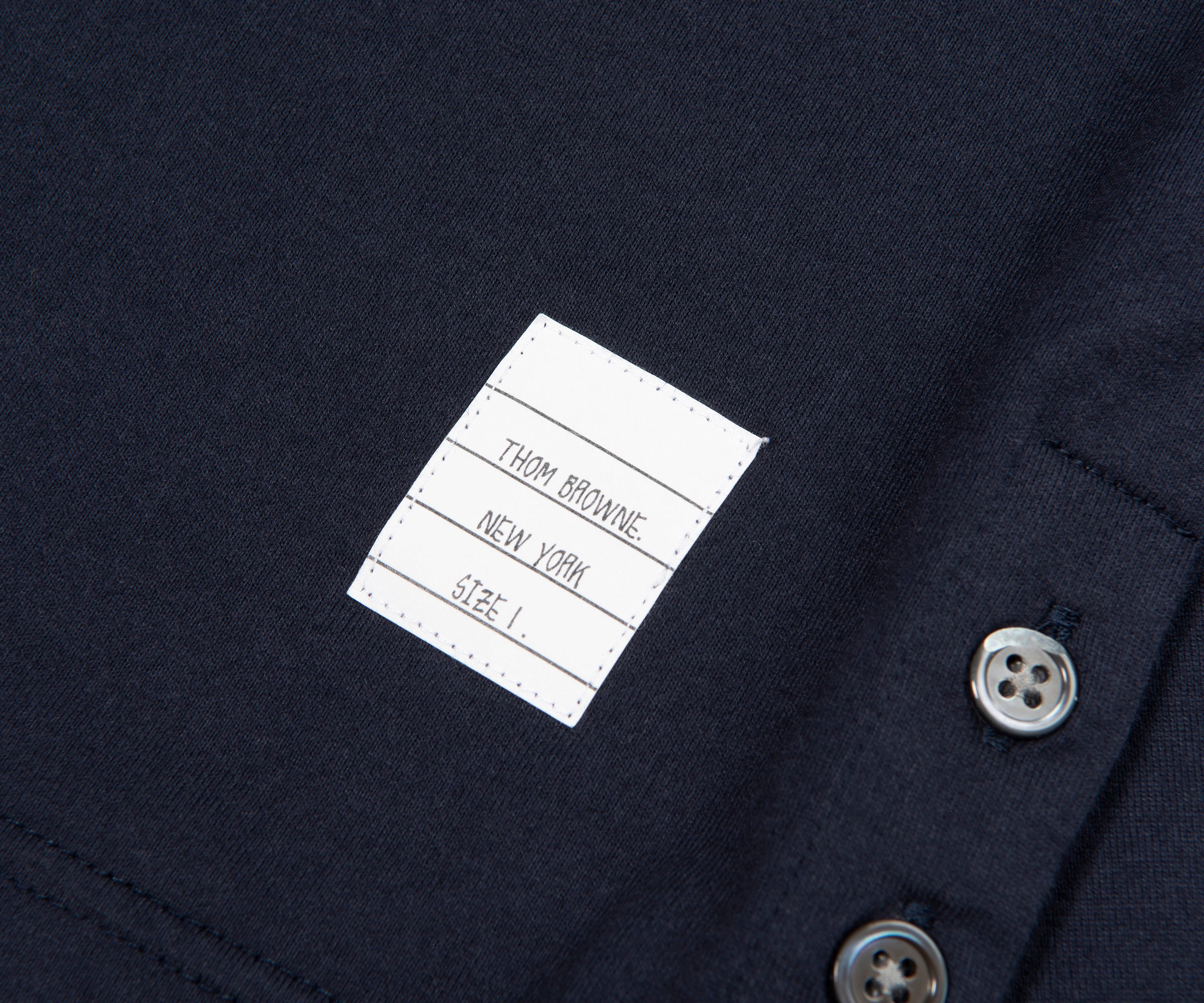 Close-up of a label on a dark fabric with buttons, featuring 'Tom Browning New York'.