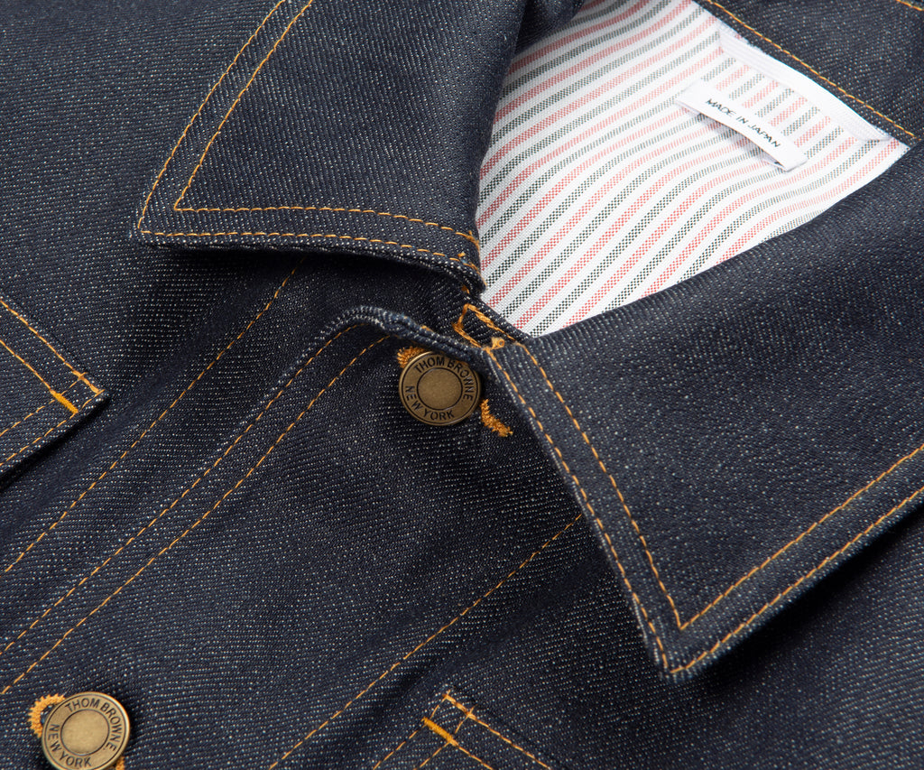 Close-up of a dark denim jacket with a button and striped lining.