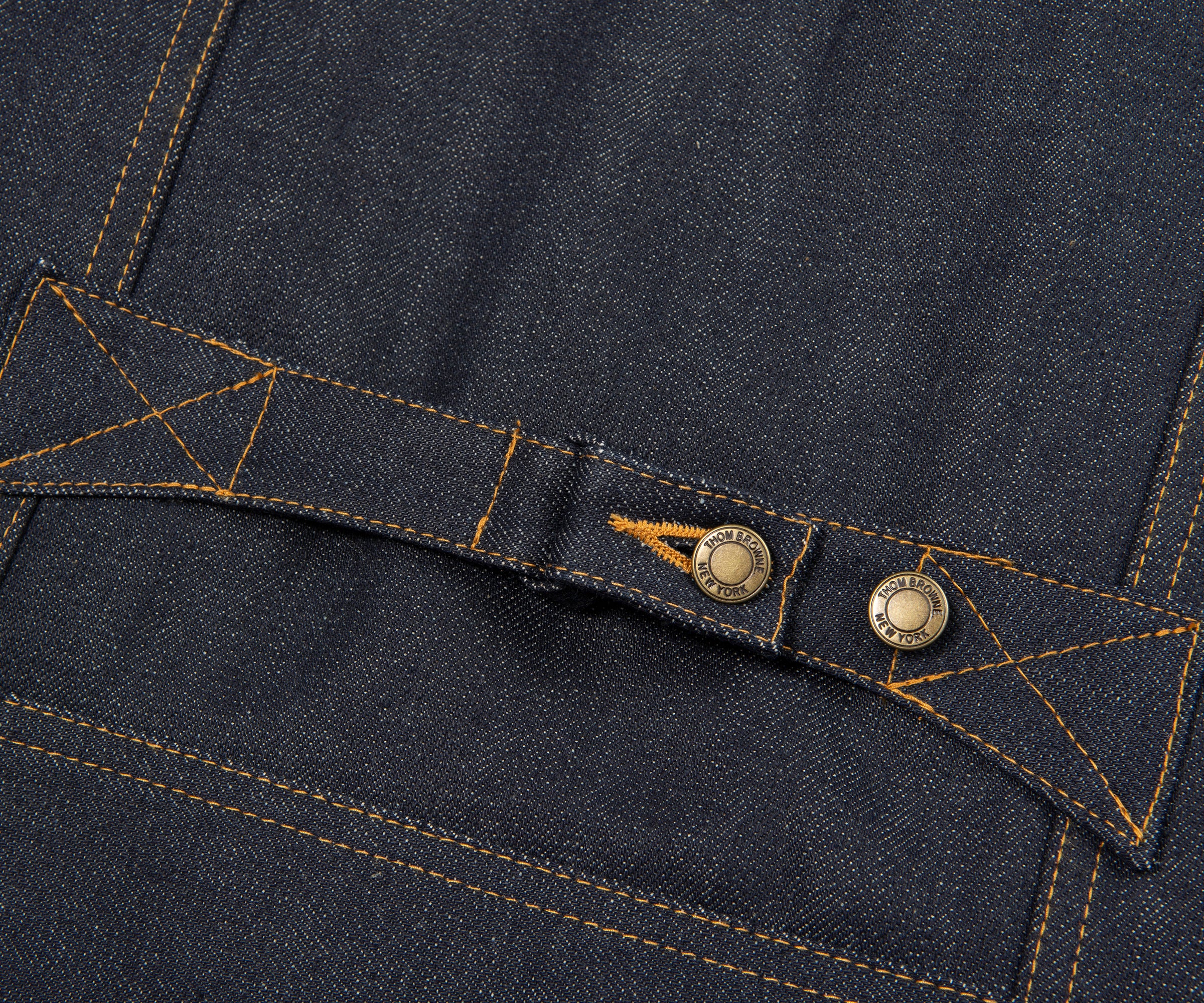 Close-up of a button on a dark blue denim fabric with stitching details.