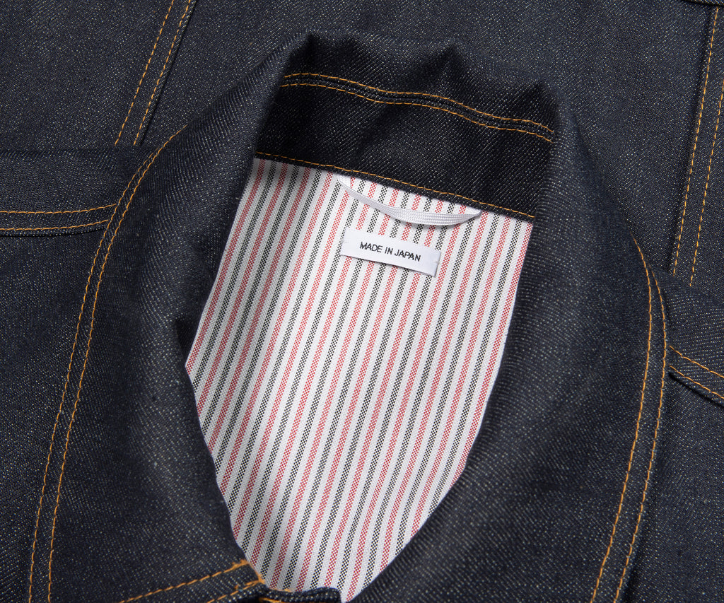 Close-up of a denim jacket with a striped pocket and 'Made in Japan' label.
