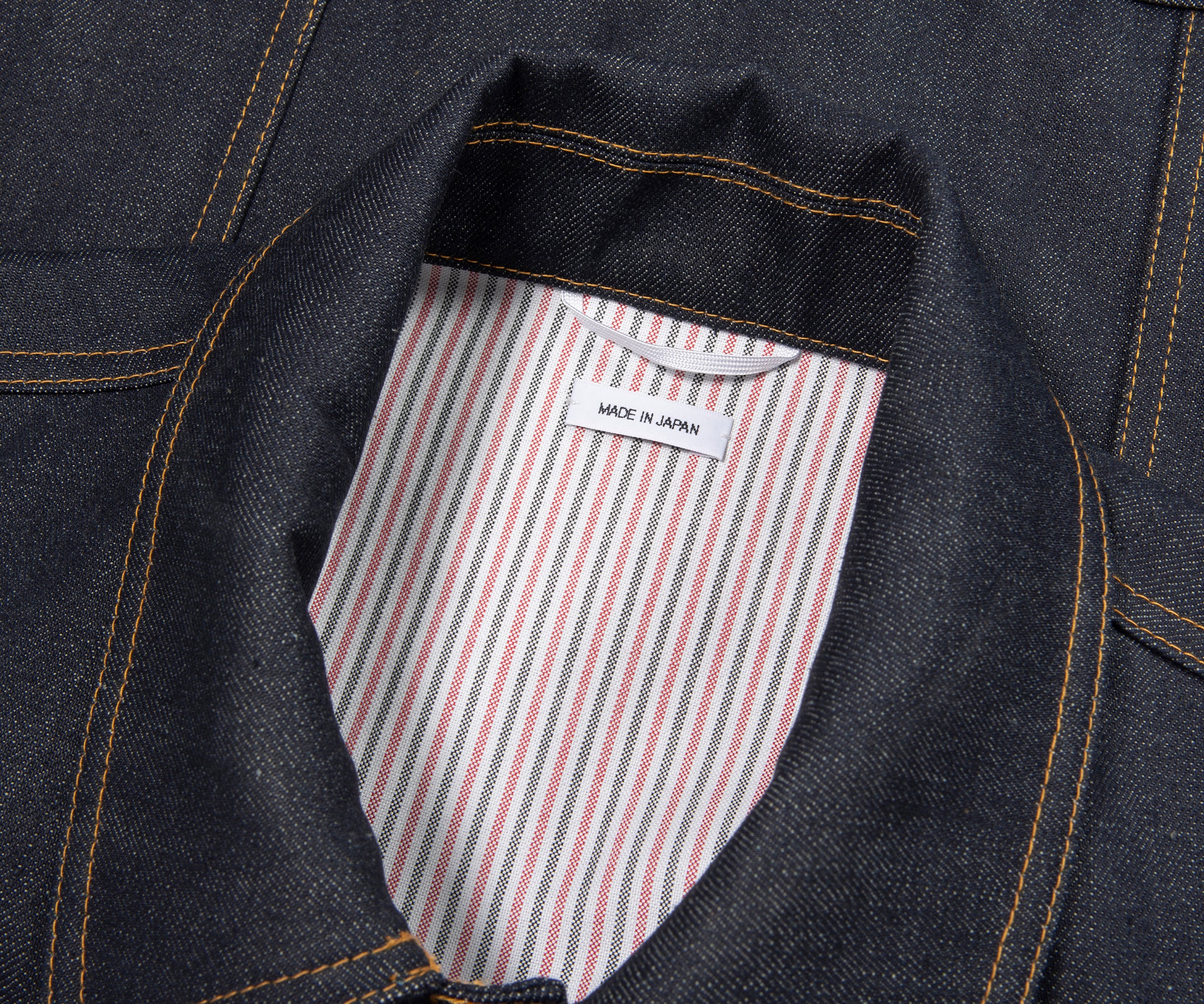 Close-up of a denim jacket with a striped pocket and 'Made in Japan' label.