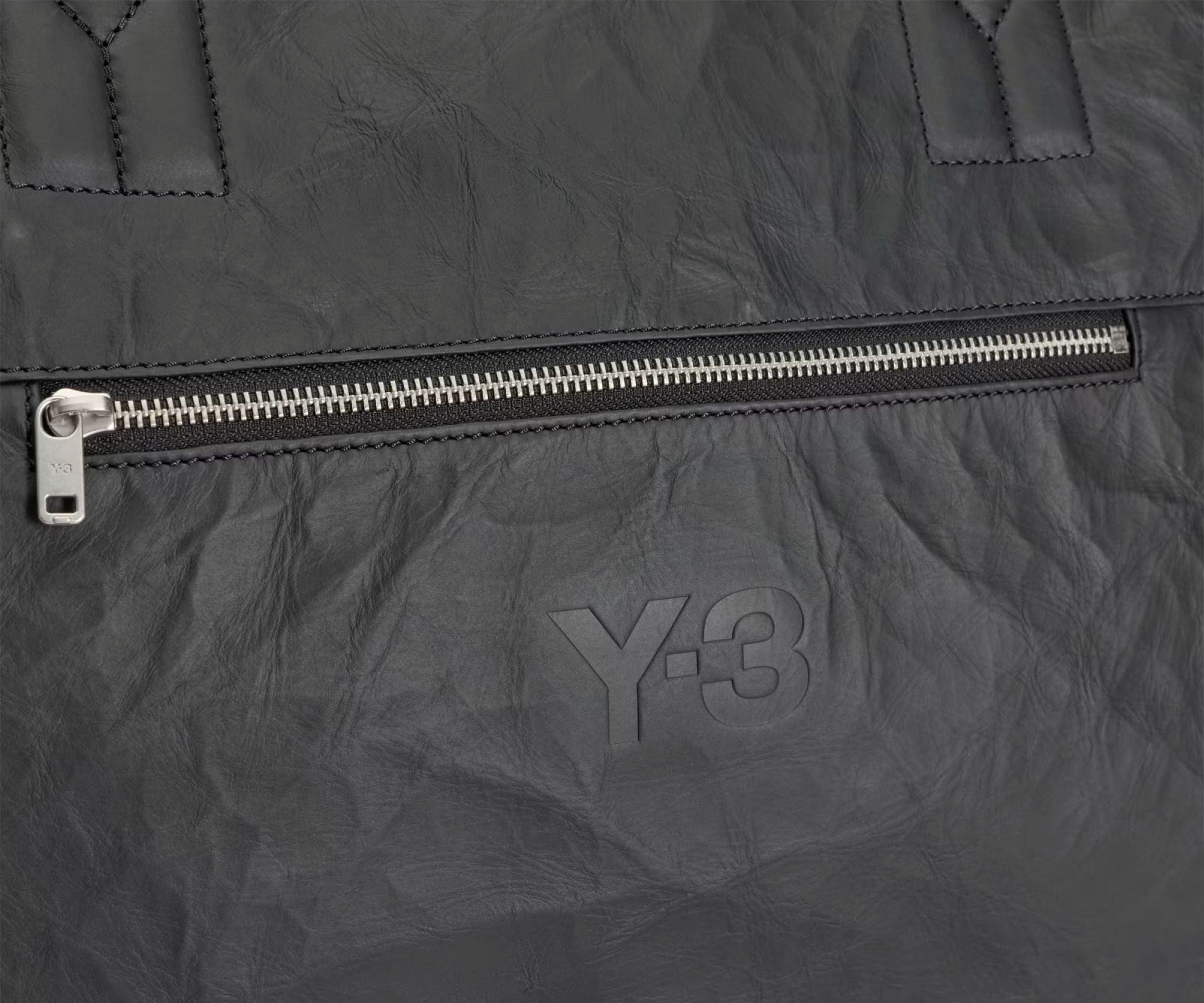 Close-up of a dark gray jacket with a zipper and Y-3 logo.