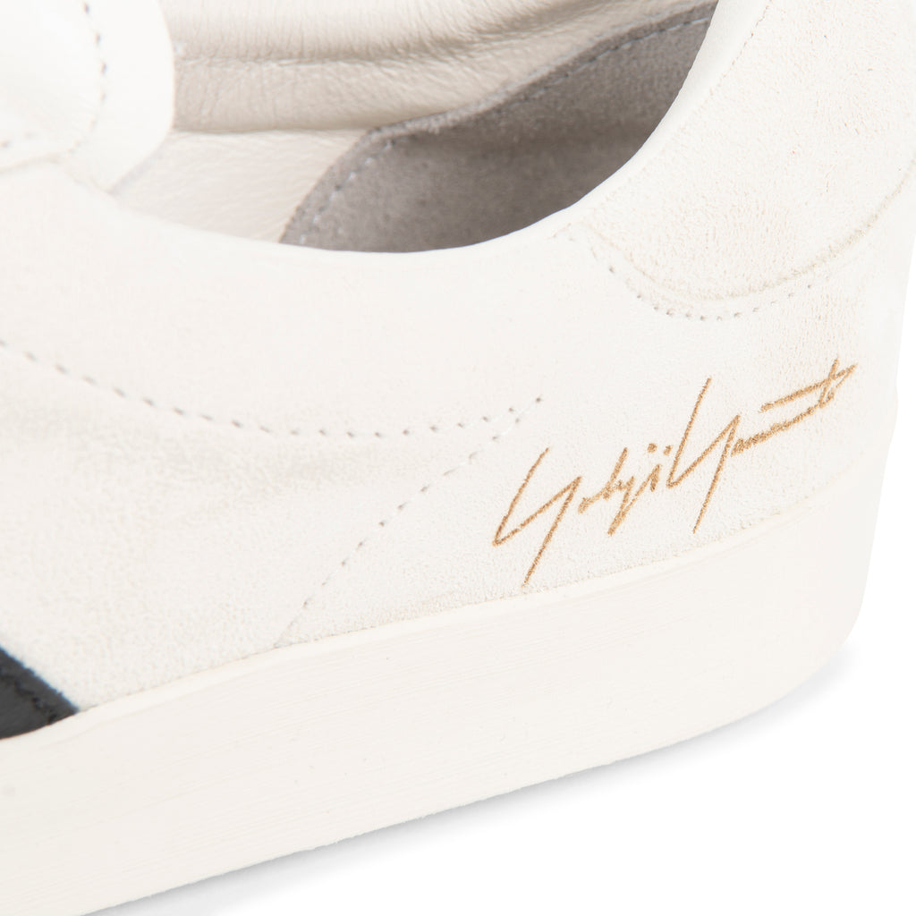 Close-up of a white sneaker with a gold logo on a white background